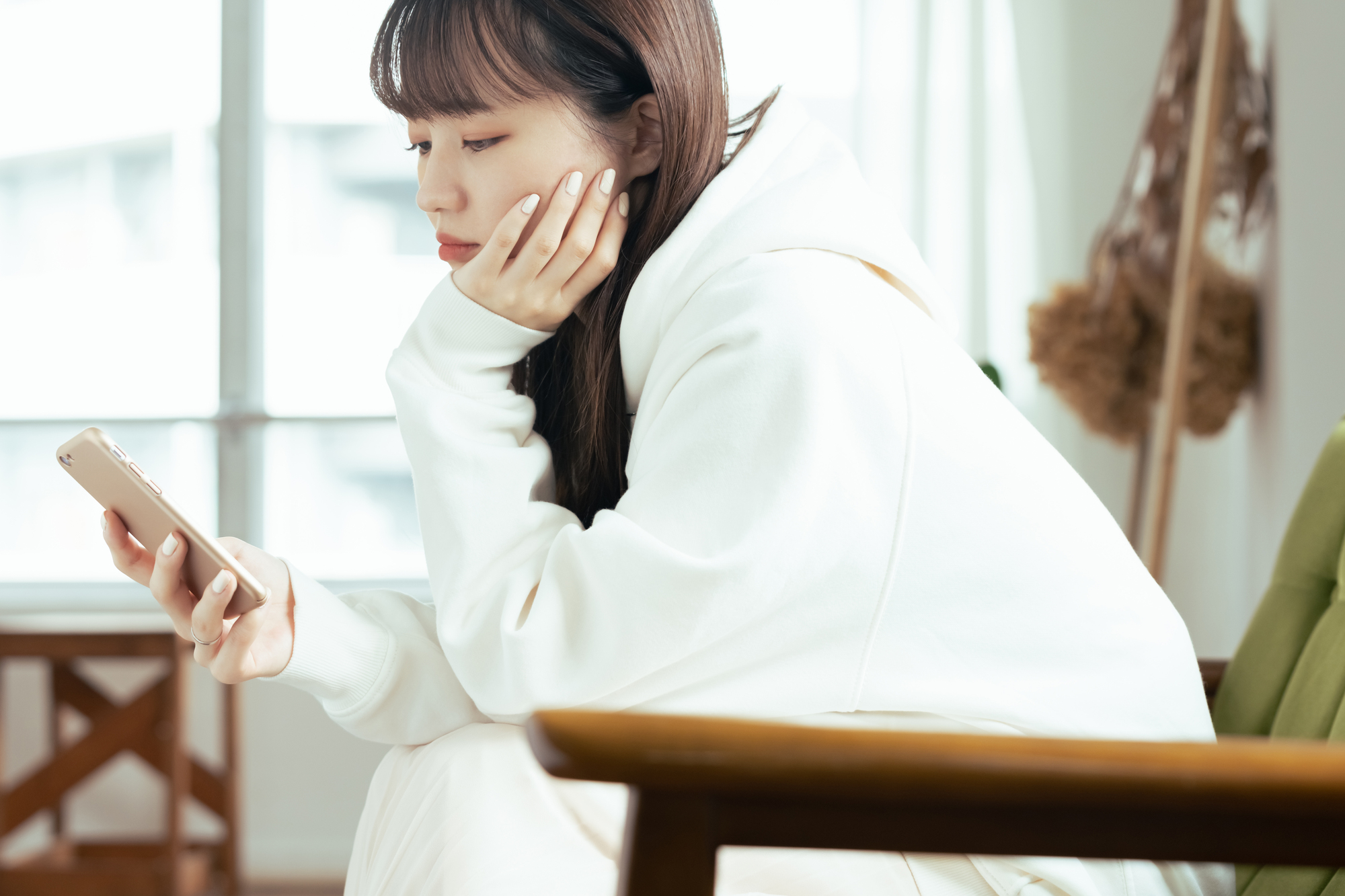 スマートフォンを見ながら考え込む女性